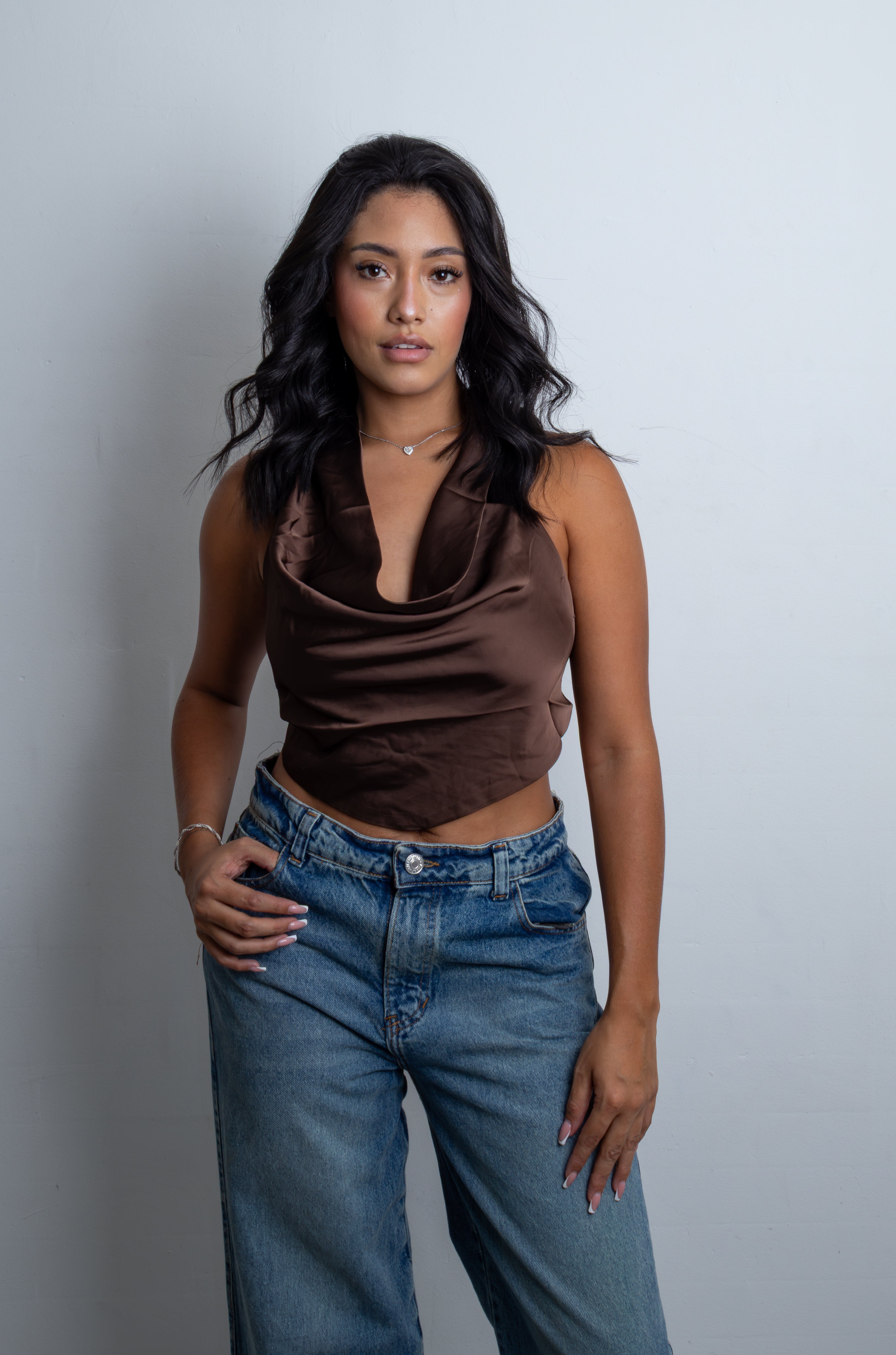Mujer luciendo el Crop Top Saphira satinado de cuello hamaca y espalda descubierta con amarre posterior, combinado con jeans.