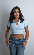 Mujer luciendo el Crop Top Verity acanalado con cuello tipo polo, botones frontales y manga corta, combinado con jeans.