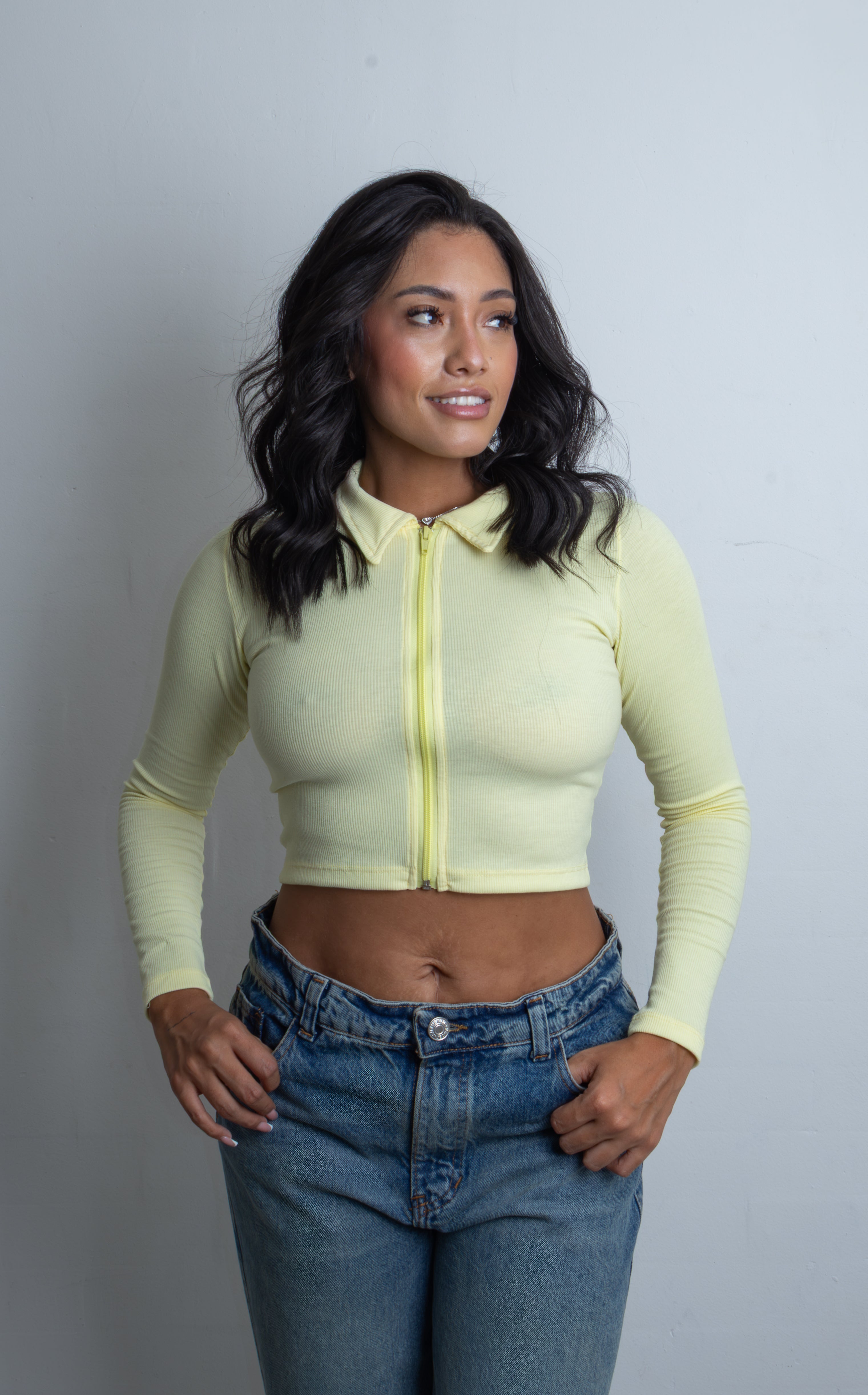 Mujer luciendo el Crop Top Chloe acanalado de manga larga con cierre frontal completo y cuello camisero, combinado con jeans.