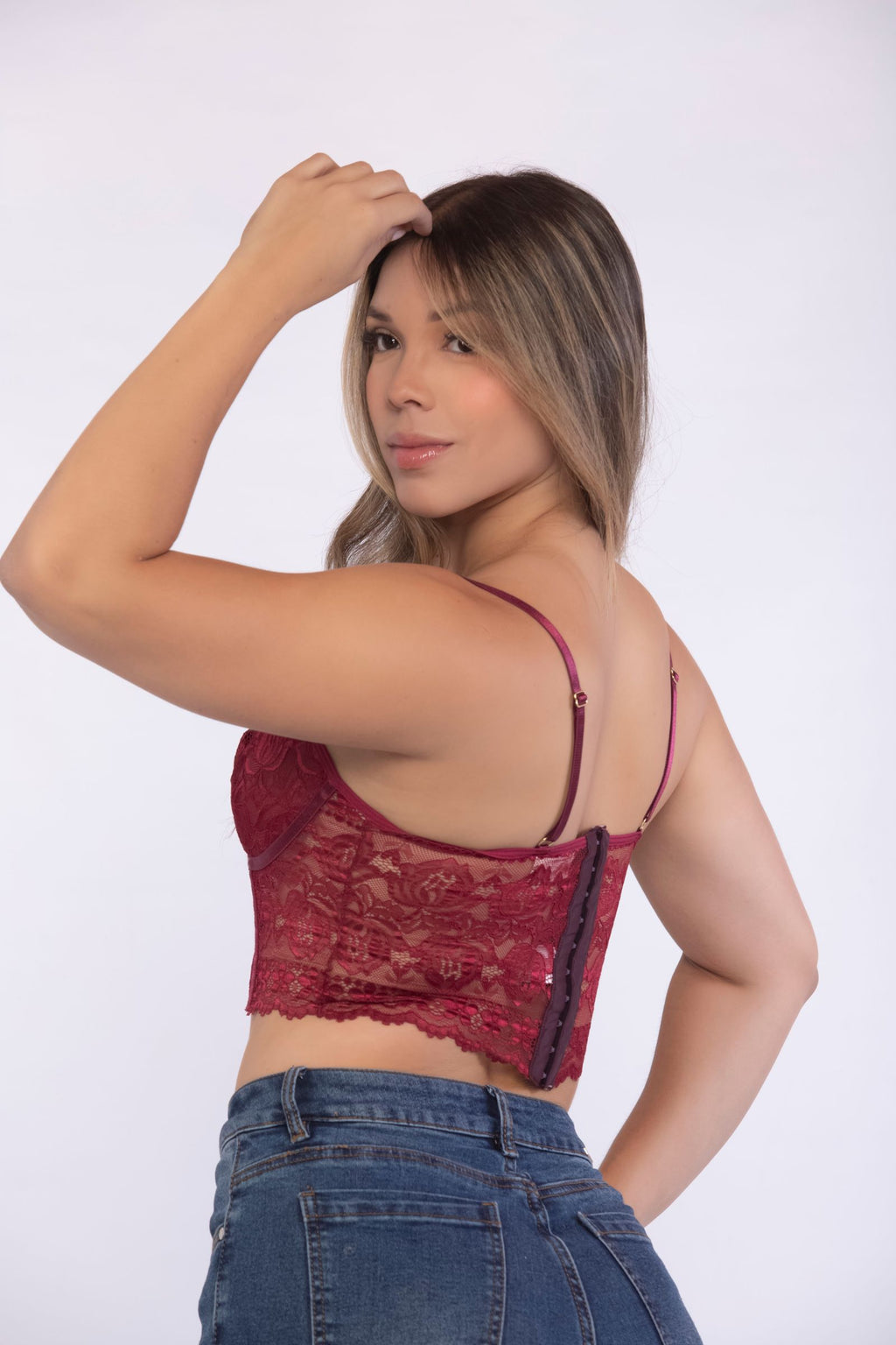 Mujer luciendo el corset de encaje rojo vino Calanthe combinado con jeans de tiro alto.