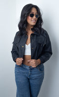 Chaqueta Cecilia negra efecto piel para mujer con cuello camisero, bolsillos con solapa, botones metálicos y tiras decorativas.