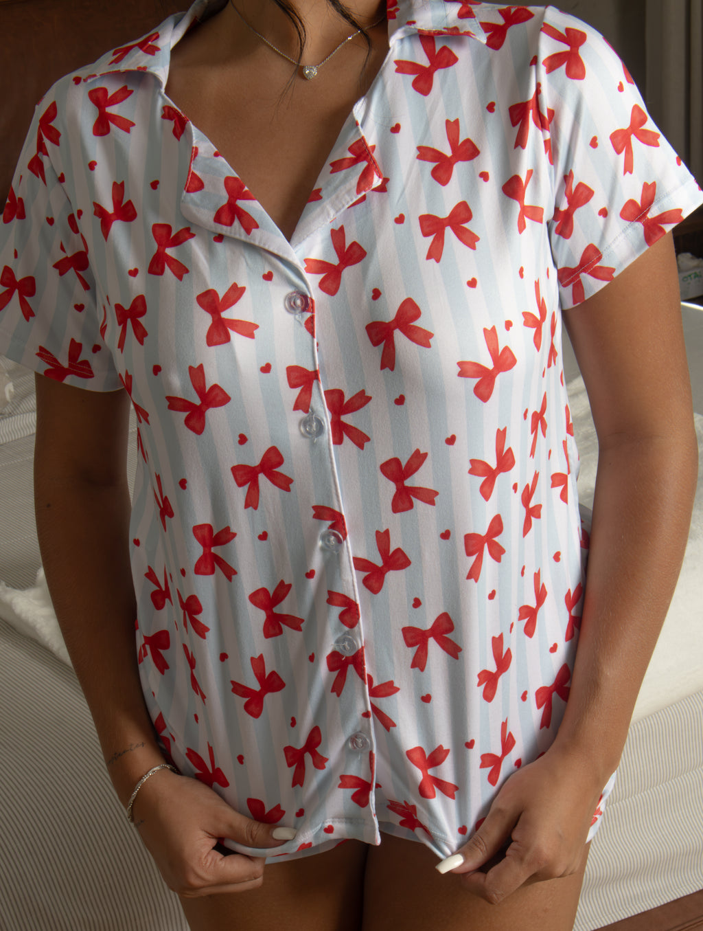 El Pijama Keira combina comodidad y un estilo femenino encantador. Su diseño de dos piezas en fondo blanco, decorado con un delicado estampado de moños rojos, incluye camiseta de manga corta y short. Perfecto para dormir, descansar y disfrutar momentos de relax en casa con un toque romántico.