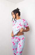 Mujer sonriente luciendo el conjunto de pijama larga Lucinda de dos piezas en color rosa con estampado de moños y corazones.